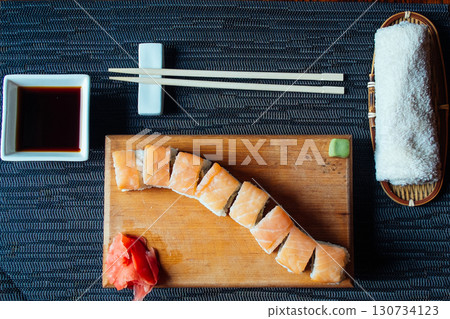 A sushi roll sits on a wooden cutting board with chopsticks and a napkin nearby 130734123