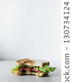 A sandwich with lettuce and meat is cut in half and placed on a white background 130734124