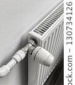 A radiator is turned off and has a white thermostat on it 130734126