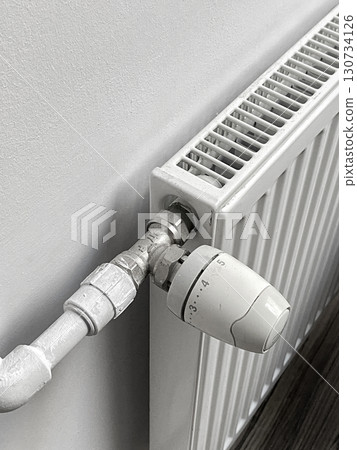 A radiator is turned off and has a white thermostat on it 130734126