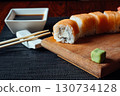 A sushi roll with a piece missing sits on a wooden board 130734128