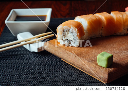 A sushi roll with a piece missing sits on a wooden board A sushi roll with a piece missing sits on a wooden board 130734128