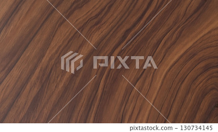 Wooden surface with a grainy texture. The wood appears to be of a darker color, possibly mahogany or oak. The grain of the wood is visible, giving the surface a natural and rustic appearance Wooden surface with a grainy texture. The wood appears to be of a darker color, possibly mahogany or oak. The grain of the wood is visible, giving the surface a natural and rustic appearance 130734145
