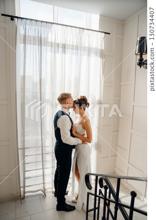 Portrait of a beautiful groom and a bride by the window 130734407