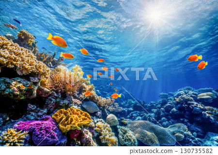 Vibrant underwater coral reef with colorful tropical fish swimming. Bright sun rays penetrate clear blue ocean water, illuminating diverse marine life. 130735582