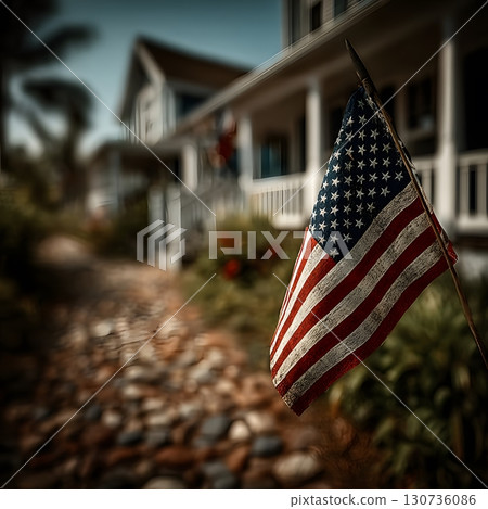 An American flag hangs prominently in front of a classic house, symbolizing national pride and heritage in a peaceful setting. 130736086