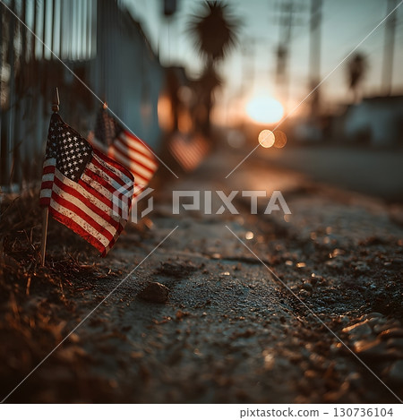 Small American flags stand along a rustic path, bathed in the golden light of a sunset, symbolizing honor and national remembrance. 130736104