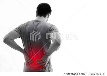A person experiencing significant lower back pain stands, holding his aching body with both hands, seeking relief from discomfort. 130736311