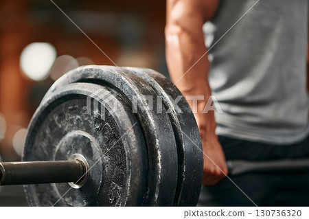 An individual performs a powerful fitness exercise, gripping a heavy barbell with plates to achieve physical fitness. 130736320