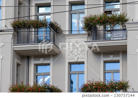 Ornate European building facade showcases classic architecture, elegant balconies with vibrant red geranium flowers, reflecting charming residential beauty and urban living 130737144