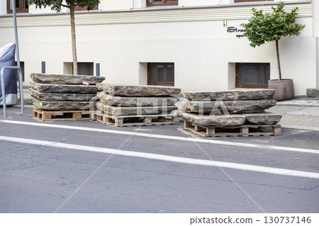 Substantial, rough natural stone paving slabs are neatly stacked on durable wooden pallets on a busy city street, ready for urban area development Substantial, rough natural stone paving slabs are neatly stacked on durable wooden pallets on a busy city street, ready for urban area development 130737146