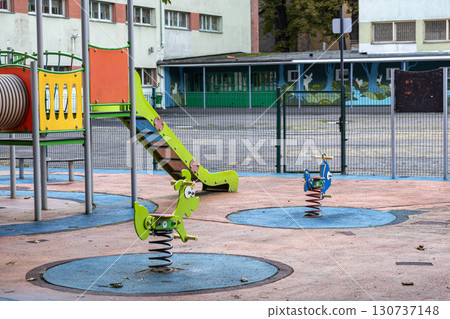 Empty urban playground featuring a vibrant slide and colorful animal spring riders, evoking quiet public space for children's recreation and outdoor education Empty urban playground featuring a vibrant slide and colorful animal spring riders, evoking quiet public space for children's recreation and outdoor education 130737148