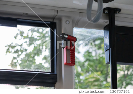 Red emergency safety hammer prominently mounted in public transport, offering vital window breaking and seatbelt cutting for passenger aid Red emergency safety hammer prominently mounted in public transport, offering vital window breaking and seatbelt cutting for passenger aid 130737161