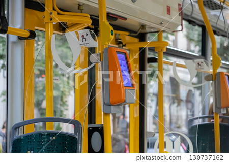 Modern public transport interior featuring bright yellow handrails, a digital ticket validation machine, and a visible otwieranie drzwi sign for urban commute 130737162