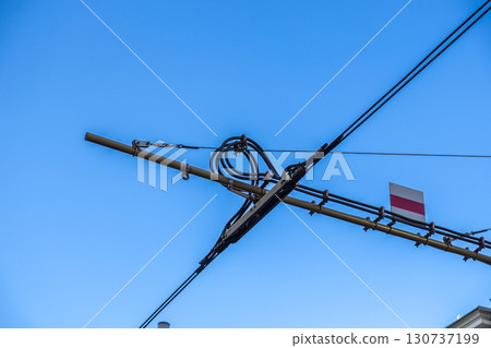 Overhead lines for urban public transport featuring complex power connections and a striped warning sign against a clear blue sky Overhead lines for urban public transport featuring complex power connections and a striped warning sign against a clear blue sky 130737199
