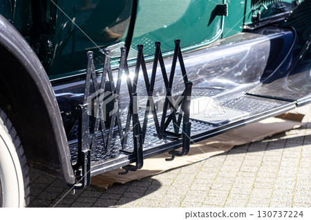 Classic green vintage car's running board featuring a gleaming collapsible luggage rack, emphasizing historical automotive design, elegance, and antique transportation aesthetic 130737224