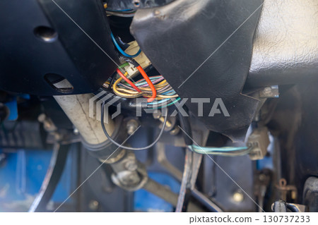 Close-up of complex tangled multi-colored electrical wiring and connectors exposed under an automobile dashboard, illustrating vehicle repair and technical maintenance 130737233