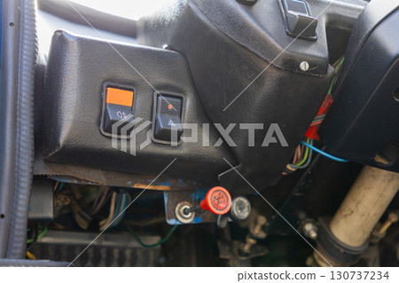 Old vehicle dashboard controls with orange fog light and hazard warning switches, exposed wiring, and a red emergency pull-knob, symbolizing automotive maintenance and utility 130737234