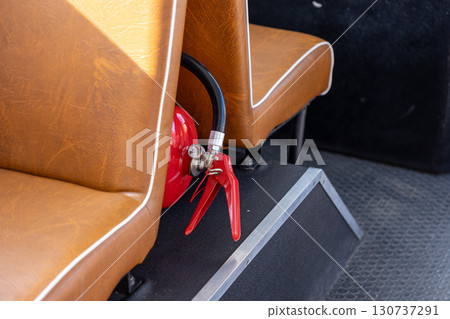 Bright red fire extinguisher securely placed between brown upholstered passenger seats, highlighting crucial safety measures and emergency readiness for public transport Bright red fire extinguisher securely placed between brown upholstered passenger seats, highlighting crucial safety measures and emergency readiness for public transport 130737291
