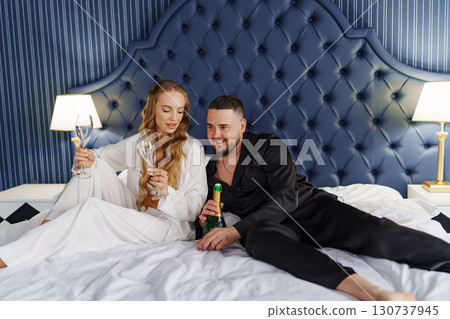 A man and a woman in silk pajamas with champagne are lying on a bed. A man and a woman in silk pajamas with champagne are lying on a bed. 130737945