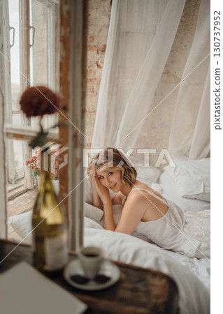 a young blonde woman in a white dress on white sheets by the window 130737952