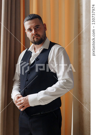 A young man in a vest and a white shirt by the window. 130737974