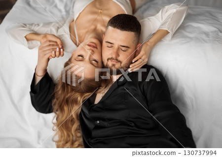 A man and a woman in silk pajamas are lying on a bed. 130737994