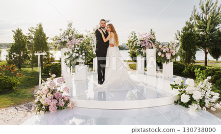 The bride and groom at the wedding ceremony site, decorated with flowers The bride and groom at the wedding ceremony site, decorated with flowers 130738000