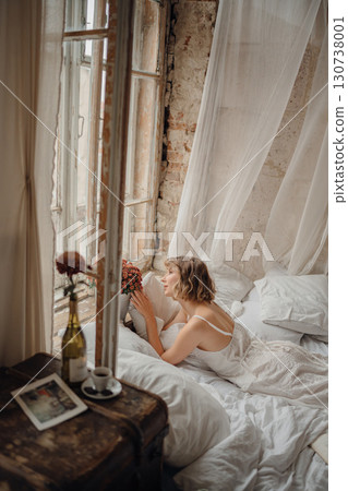 a young blonde woman in a white dress on white sheets by the window 130738001
