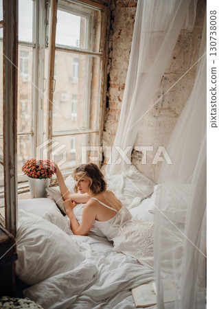 a young blonde woman in a white dress on white sheets 130738008