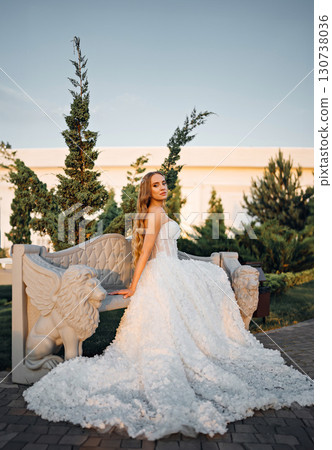 Beautiful bride with long blonde hair on a stone bench in an evening park.  130738036