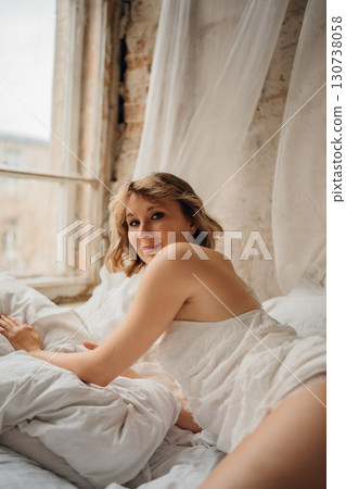 an attractive blonde woman in a white dress on white sheets an attractive blonde woman in a white dress on white sheets 130738058