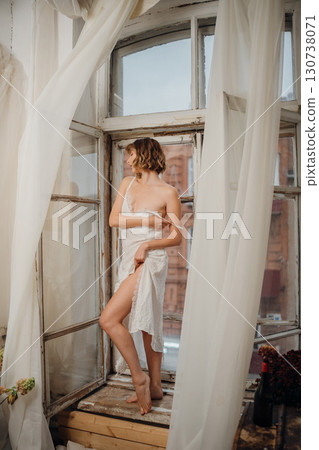 Beautiful and slender young woman in a long white dress with bare feet.  130738071