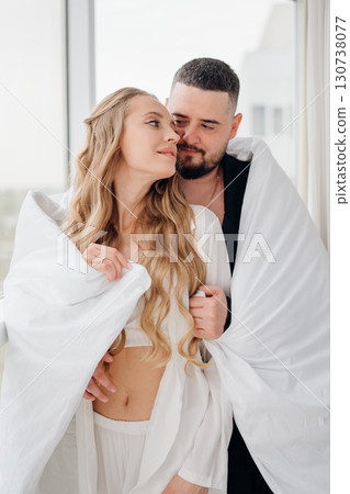 A gentle and romantic man and woman wrapped in a blanket on the windowsill A gentle and romantic man and woman wrapped in a blanket on the windowsill 130738077