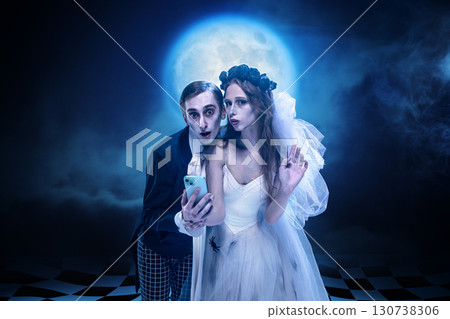 Gothic bride and groom staring at smartphone with spooky expression under moonlight 130738306