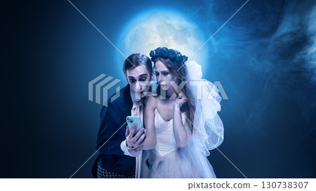 Surreal gothic wedding couple looking at smartphone under full moon Surreal gothic wedding couple looking at smartphone under full moon 130738307