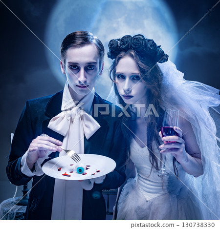 Pale gothic bride and groom with surreal food element in moonlit scene 130738330