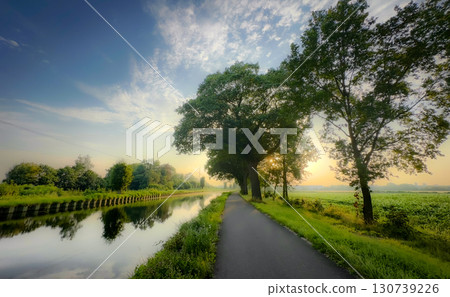 A Scenic River Pathway at Sunset, Surrounded by Lush Greenery and Flourishing Nature 130739226