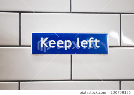 Keep Left safety sign on white subway tiles - blue wayfinding for pedestrian traffic flow Keep Left safety sign on white subway tiles - blue wayfinding for pedestrian traffic flow 130739335