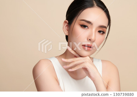A beautiful young Asian woman with clean, fresh skin against a beige background. Skincare, facial treatment, cosmetology, beauty, and spa. An elegant portrait of an Asian woman. 130739880