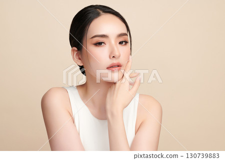 A beautiful young Asian woman with clean, fresh skin against a beige background. Skincare, facial treatment, cosmetology, beauty, and spa. An elegant portrait of an Asian woman. 130739883