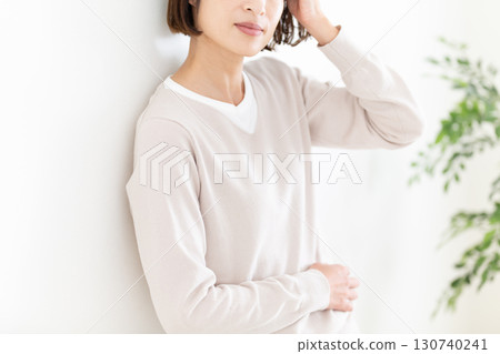 一位穿著休閒服的中年婦女靠在窗邊的白牆上 一位穿著休閒服的中年婦女靠在窗邊的白牆上 130740241