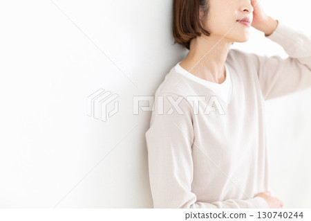 A middle-aged woman in casual clothes leaning against a white wall by the window A middle-aged woman in casual clothes leaning against a white wall by the window 130740244