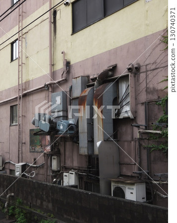 The side of the building is covered with miscellaneous pipes and rusty ducts. The side of the building is covered with miscellaneous pipes and rusty ducts. 130740371