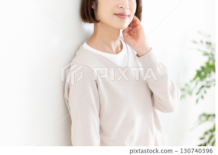 一位穿著休閒服的中年婦女靠在窗邊的白牆上 一位穿著休閒服的中年婦女靠在窗邊的白牆上 130740396
