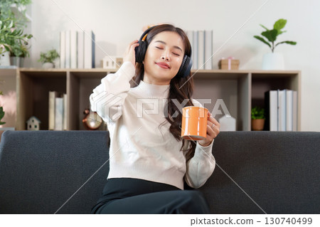 Music and Relaxation. Young woman enjoying music with headphones and coffee at home. Music and Relaxation. Young woman enjoying music with headphones and coffee at home. 130740499
