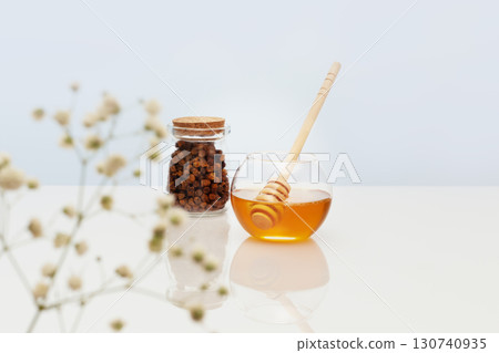 Healthcare composition with propolis and honey in glass jars with honey dipper on a white table with reflection and flowers. Bee products are an natural, folk medicine. Immune boosting products 130740935