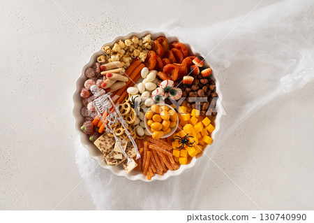 Halloween funny charcuterie board with sliced pumpkins, chocolate candy, spider, crackers on white background. View from above. 130740990