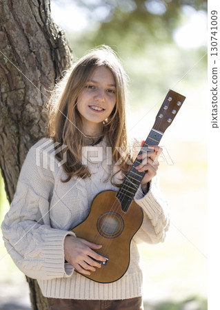 Young musician holding ukulele, posing by tree in nature Young musician holding ukulele, posing by tree in nature 130741009