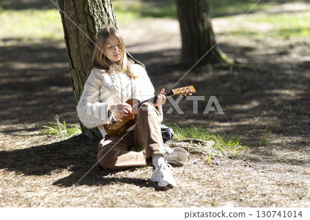Young woman playing ukulele under tree in forest 130741014